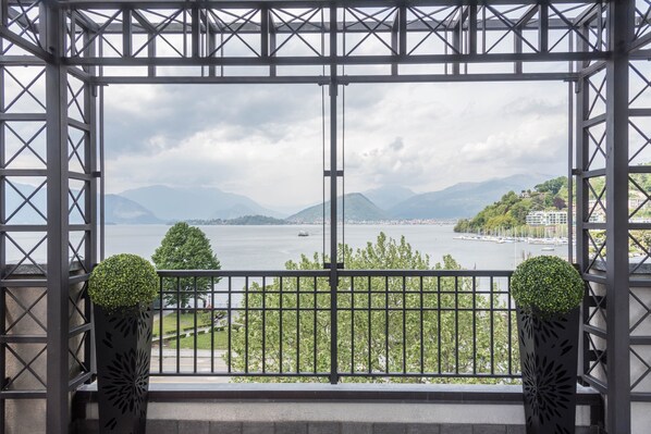 A balcony with a metal railing, two potted plants, and a view of a body of water with mountains in the background.