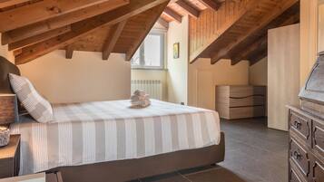 A bedroom with a bed, wooden ceiling beams, a dresser, and a window.