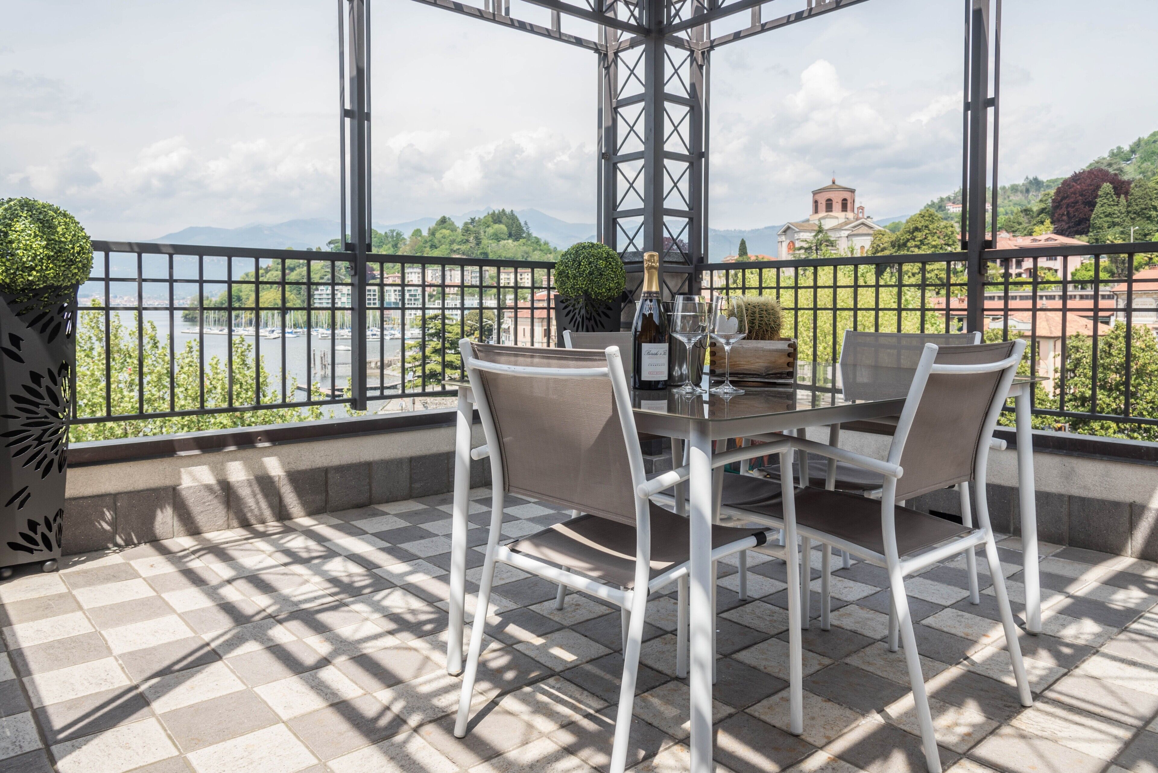 A terrace with a table set for two, a bottle of champagne, and a view of a body of water and mountains.