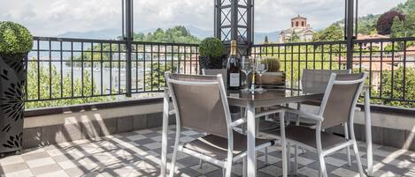 A terrace with a table set for two, a bottle of champagne, and a view of a body of water and mountains.