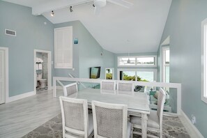 A dining area with a white table and chairs, a ceiling fan, and a view of the outdoors.