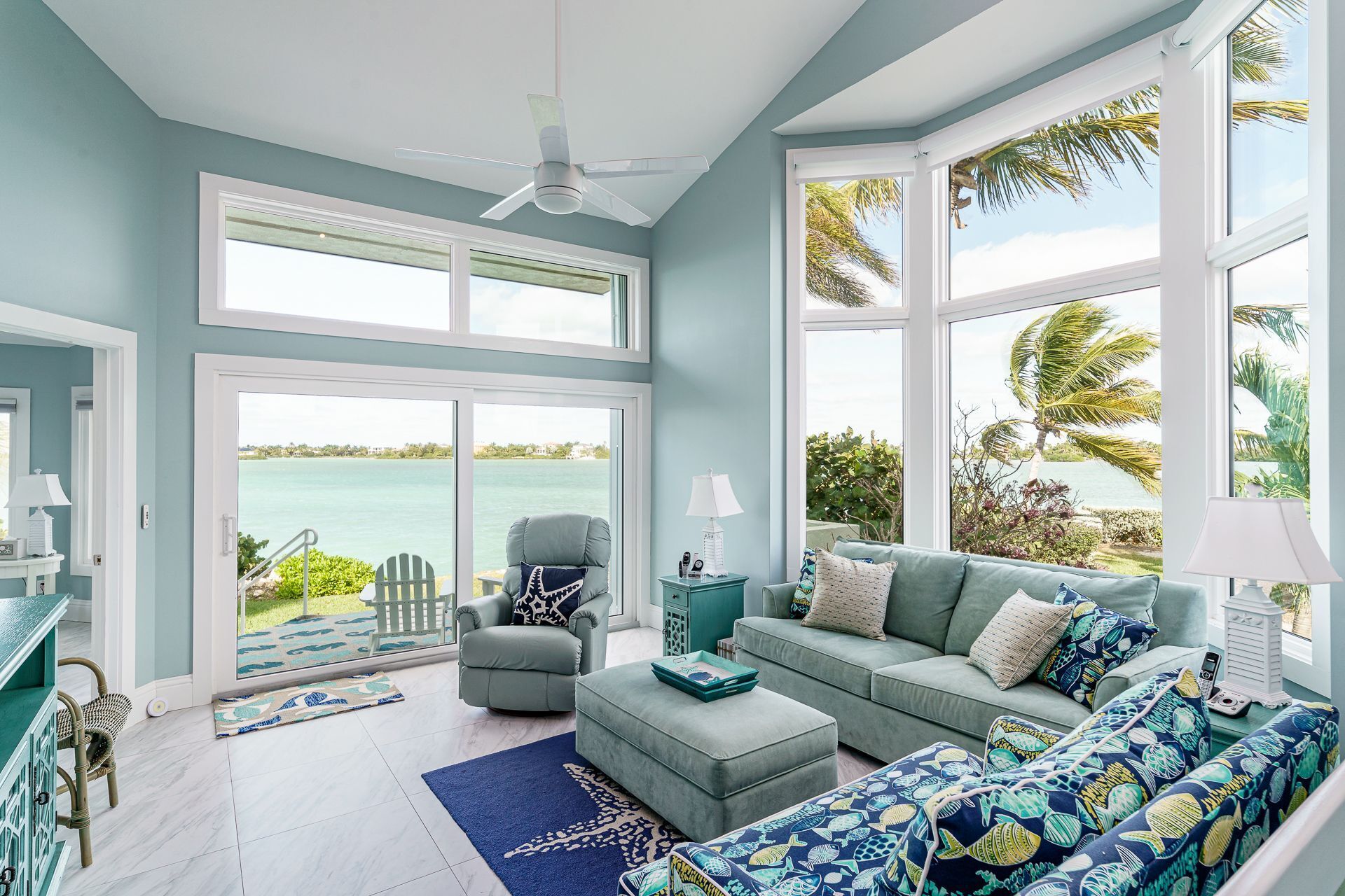 A spacious living room with a large window overlooking a body of water, a ceiling fan, and a view of the outdoors.