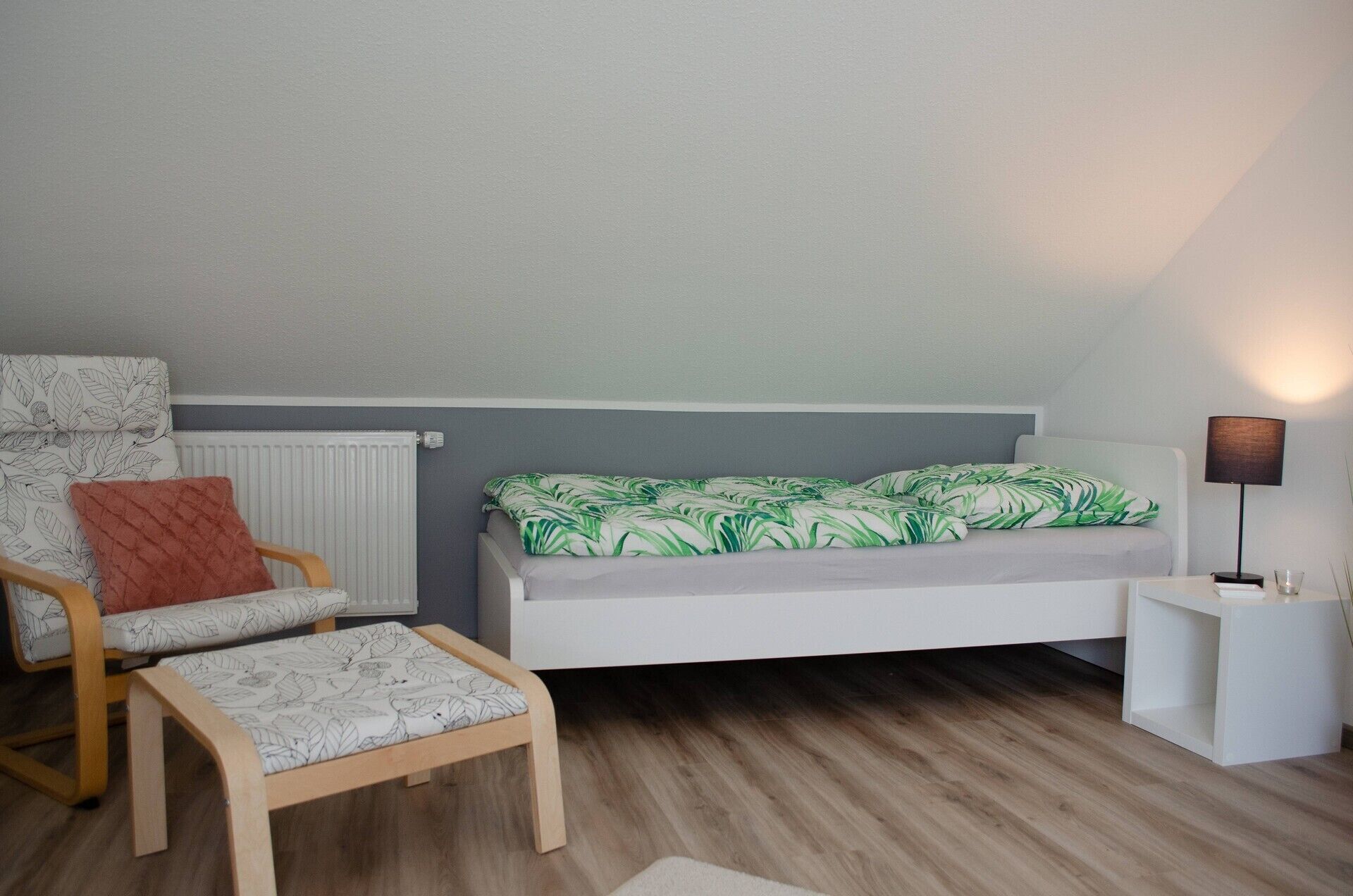 A bedroom with a bed, a chair, a small table, and a lamp.