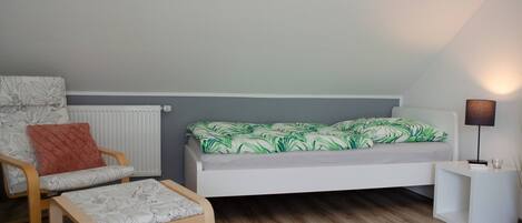 A bedroom with a bed, a chair, a small table, and a lamp.