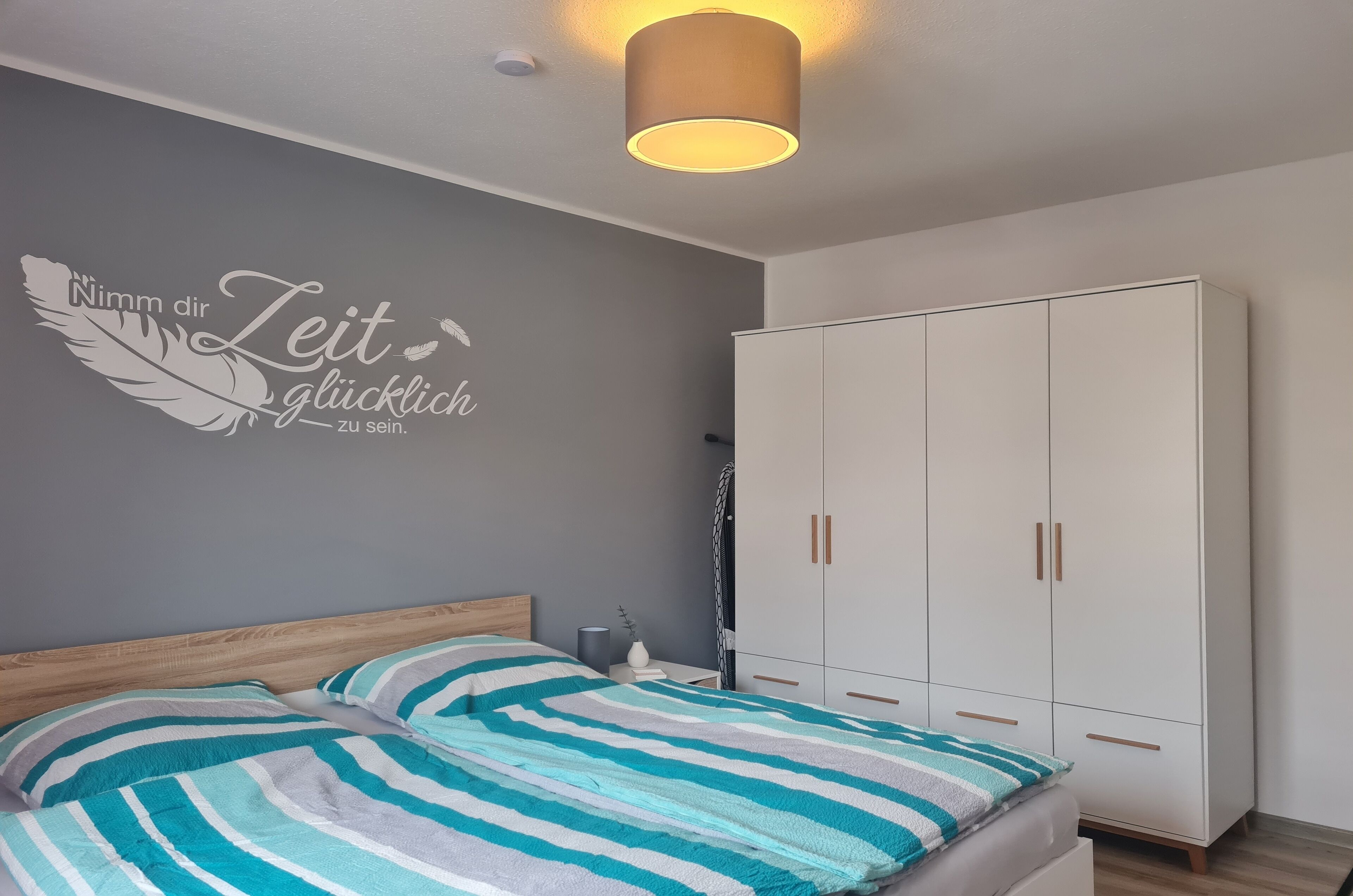 Une chambre à coucher comprenant un lit, une armoire et un mur orné d’une citation inspirante.