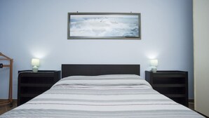 A bedroom with a bed, two bedside tables, a nightstand, a framed picture on the wall, and a wooden chair. - Silvia Loft on Hill between Green & White Coast (Portoferraio)