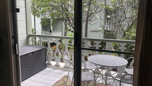 A balcony with a white metal table and chairs, a wicker bench, and a view of a street with trees and a building labeled "LANAS".