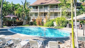 A hotel with a swimming pool, lounge chairs, and tropical landscaping.