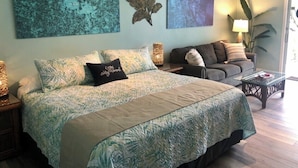A bedroom with a large bed, a sofa, and a coffee table. There are wall art pieces and a plant.