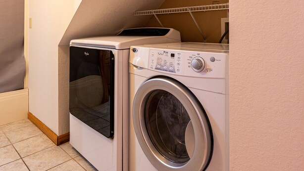 Een compacte was- en droogcombinatie in een hoek van een kamer met betegelde vloer.