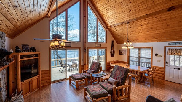 A spacious cabin interior with a high ceiling, large windows, a wooden dining area, and a stone fireplace. - Ridgetop Lakeview - Bedroom Cabin on Lake Nantahala w/ Private Deck (Topton)