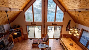 A cozy cabin interior with a high ceiling, large windows, a fireplace, and a dining area. - Ridgetop Lakeview - Bedroom Cabin on Lake Nantahala w/ Private Deck (Topton)