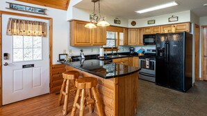 A kitchen with wooden cabinets, a black refrigerator, and a large island with stools. - Ridgetop Lakeview - Bedroom Cabin on Lake Nantahala w/ Private Deck (Topton)