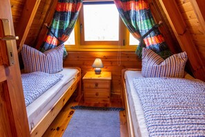 Um quarto de sótão aconchegante com duas camas de solteiro, uma pequena mesa de cabeceira de madeira e uma janela com cortinas coloridas.