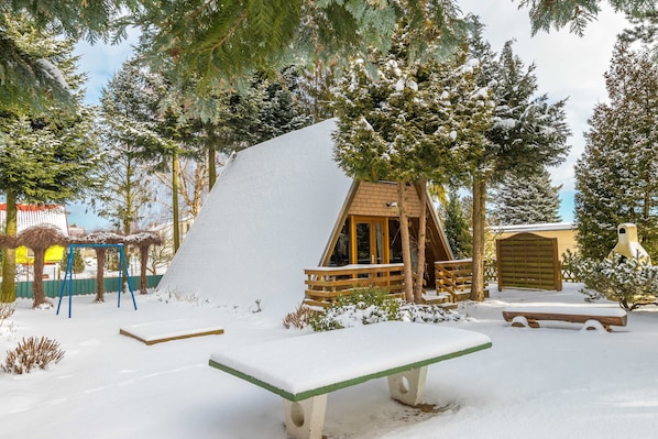 A snow-covered outdoor area with a wooden play structure, a bench, and a small wooden building.