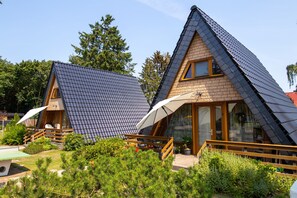 Two triangular-roofed cabins with wooden railings, a covered outdoor seating area, and a garden with small trees. - Finnish Cabin 2 - Finnish Cabins in Freest (Kröslin)