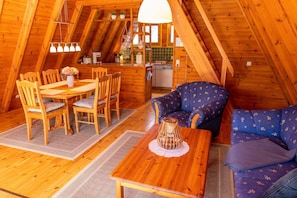 A cozy wooden interior with a dining table, chairs, a sofa, and a kitchen area.