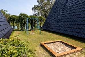 A garden with a swing set, a wooden planter box, and a metal roof structure.