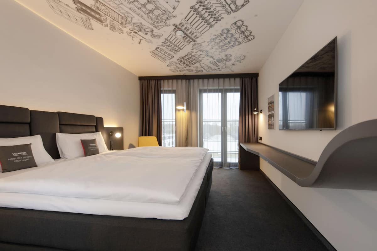 Quarto de hotel moderno com uma cama grande, televisão de tela plana e teto com esboços industriais.