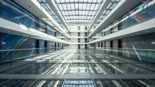 Ein modernes Atrium mit Glasdecke, spiegelnden Böden und einer zentralen Treppe.