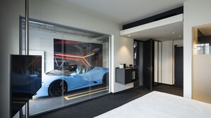 Ein modernes Hotelzimmer mit einem großen Bett, einer Glaswand, in der sich ein Auto spiegelt, einem Schreibtisch und einem Fernseher.