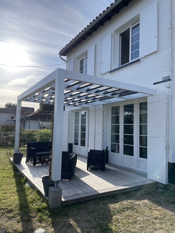 A white house with a covered patio area featuring outdoor furniture and a pergola.