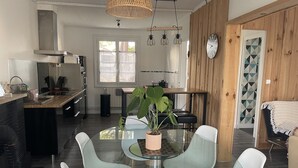 Een moderne keuken met een eethoek, met een ronde glazen tafel, witte stoelen en een potplant.