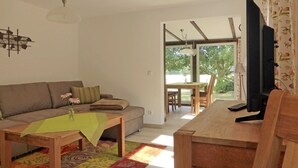 A living room with a sofa, a coffee table, a TV, and a dining area with a table and chairs. - Ferienwohnung 1 - Ferienhaus am Waldessaum (Fuhlendorf)