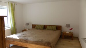 A bedroom with a wooden bed, two nightstands, a window with curtains, and a bedside table with a lamp and flowers. - Ferienwohnung 1 - Ferienhaus am Waldessaum (Fuhlendorf)
