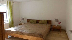 Un dormitorio con cama de madera, dos mesitas de noche con lámparas, una ventana con cortinas y suelo de madera.