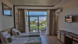 A hotel room with two beds, a desk, a TV, and a balcony with outdoor furniture. - Menabe'l (Antsirabe)