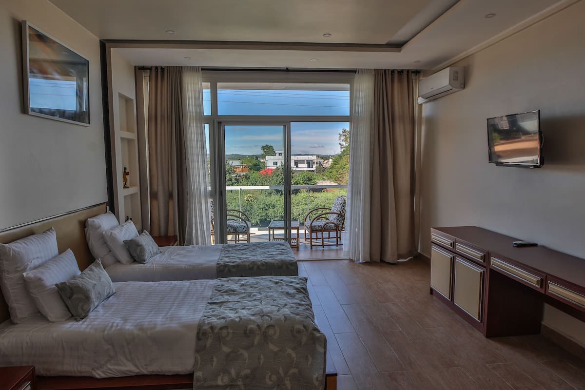 A hotel room with two beds, a desk, a TV, and a balcony with outdoor furniture.