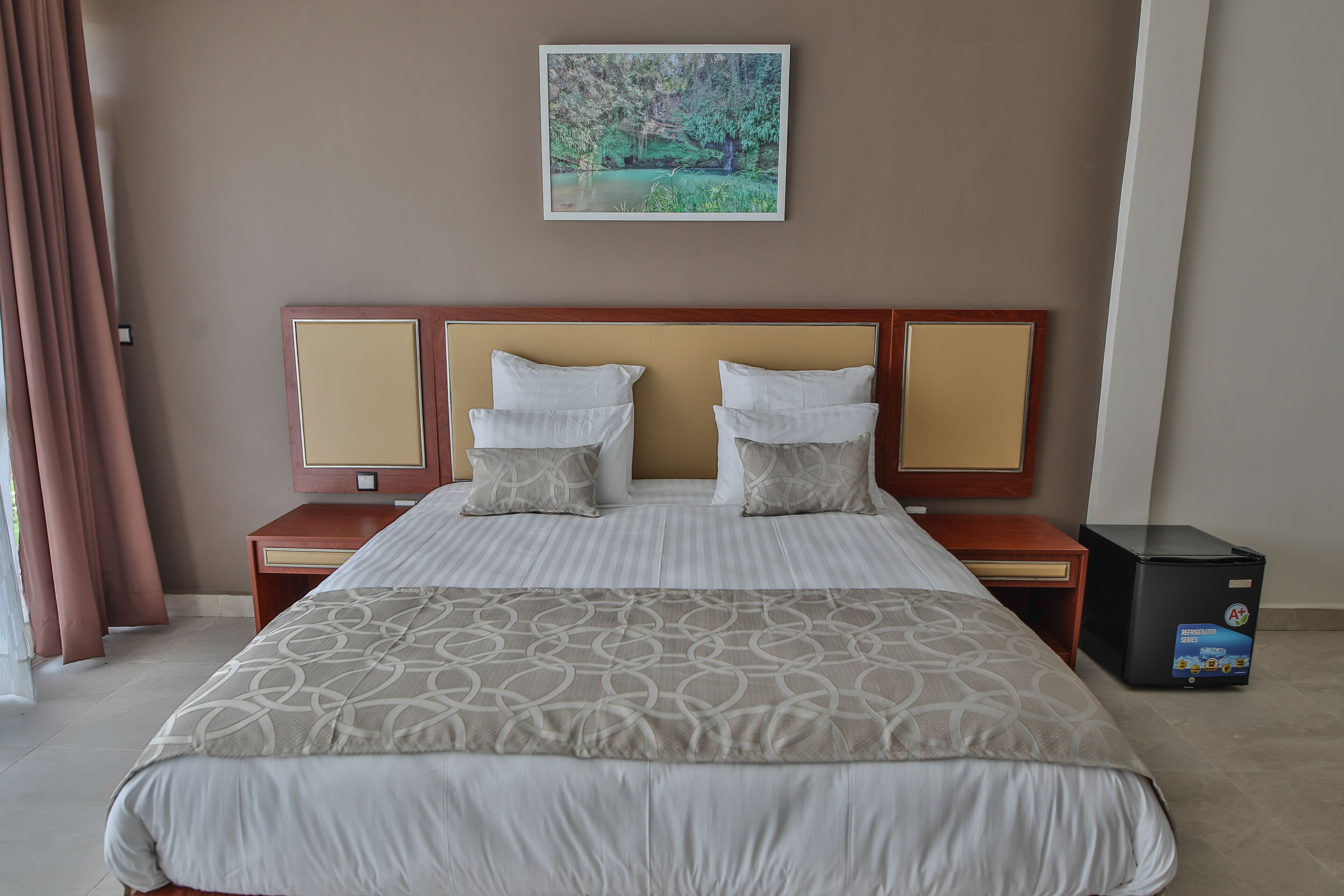 A hotel room with a large bed, two bedside tables, a nightstand, a wall-mounted TV, and a small refrigerator.