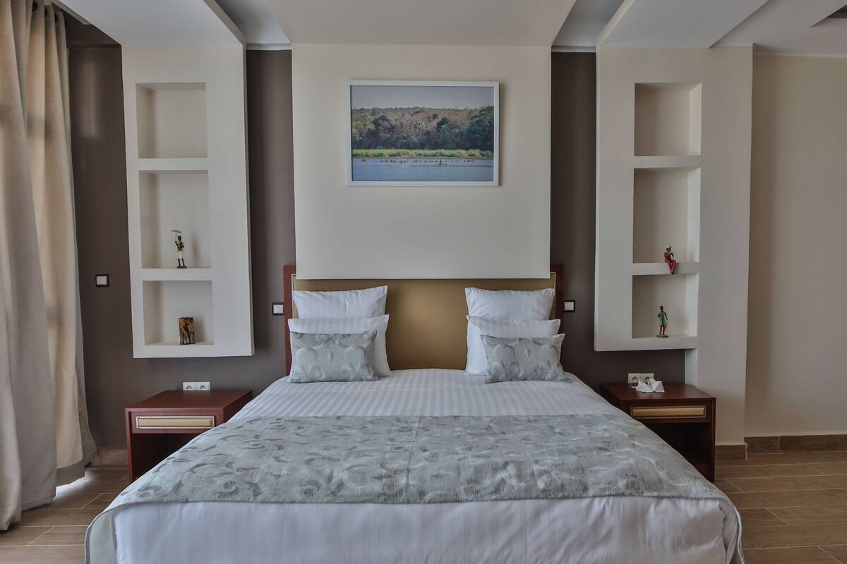 A hotel room with a large bed, two nightstands, a headboard with shelves, and a framed picture on the wall.