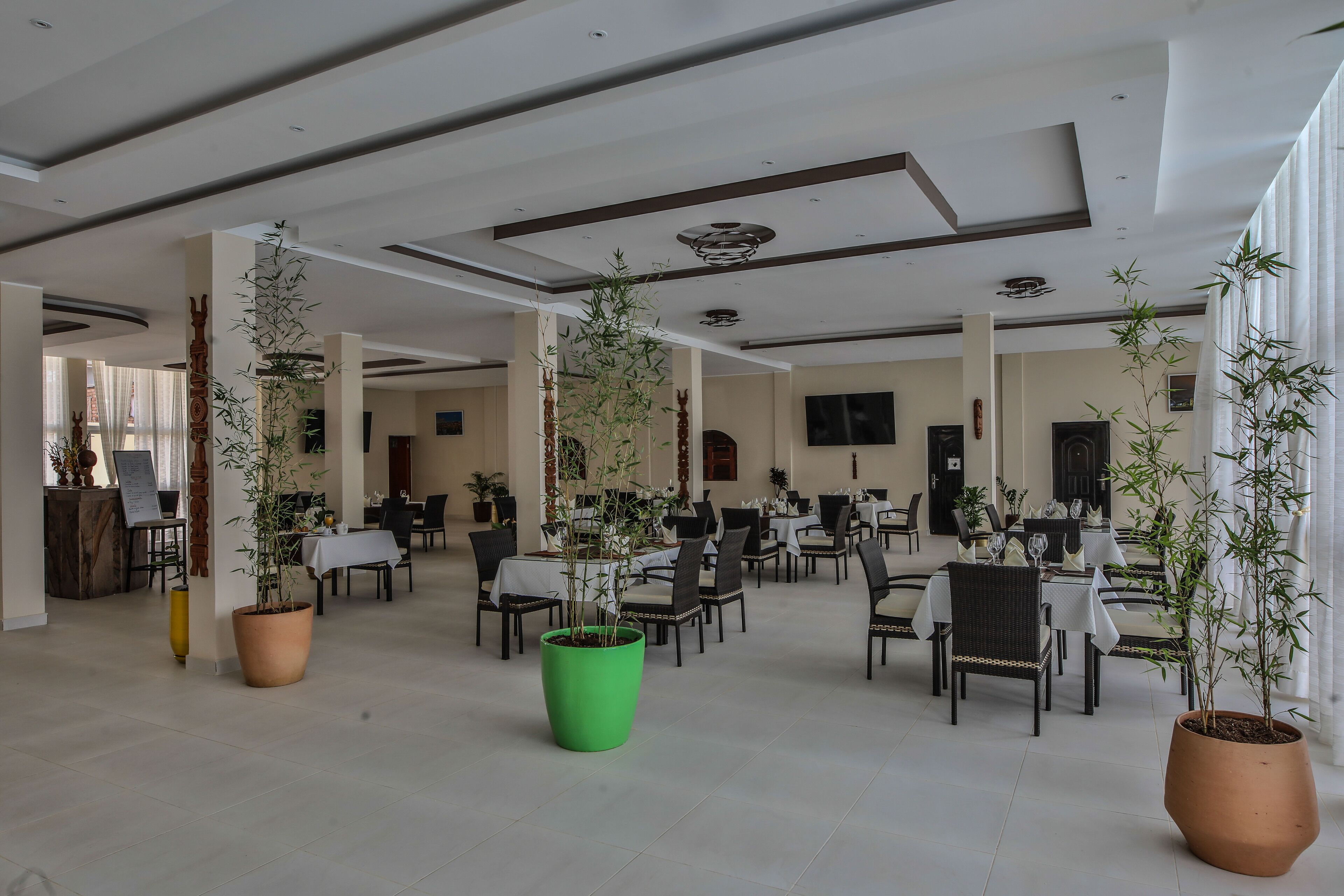 A spacious indoor area with multiple tables and chairs, potted plants, and a high ceiling with recessed lighting.