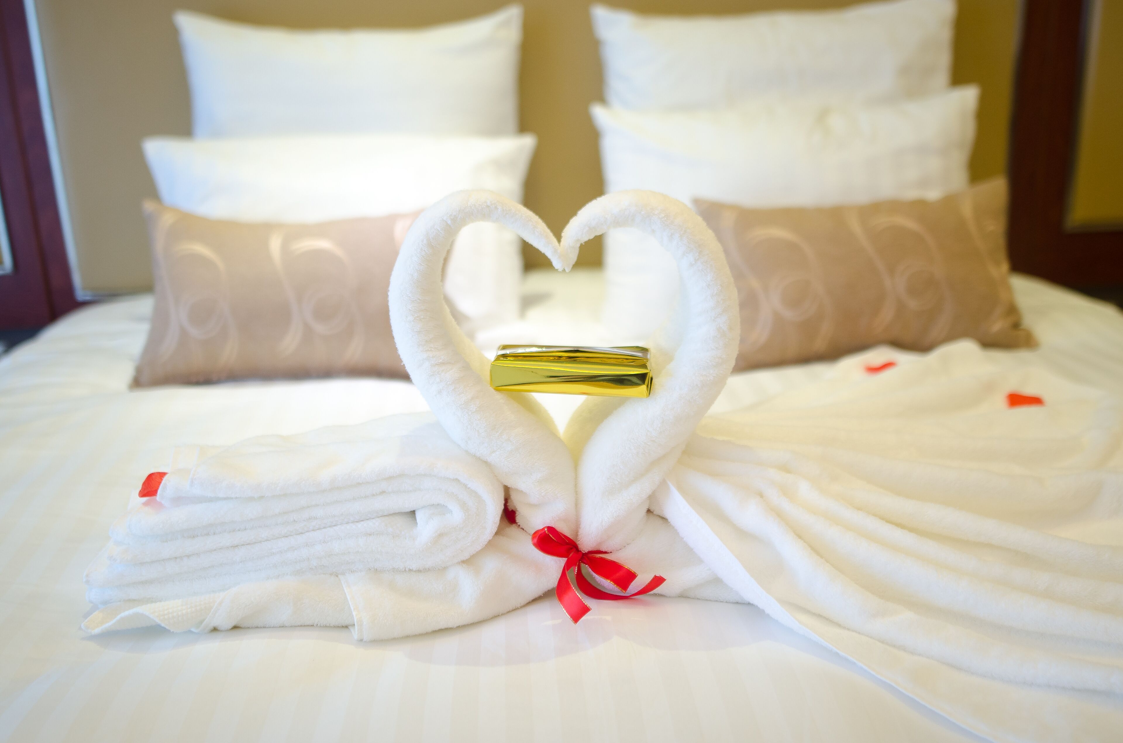 Un letto con lenzuola bianche e un'accattivante disposizione di asciugamani a forma di cuore, con un oggetto dorato al centro.