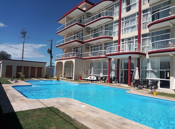 A hotel with a swimming pool, outdoor seating, and multiple balconies.