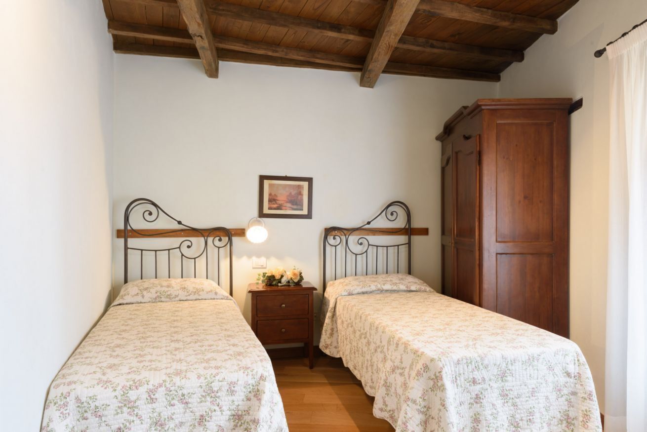 Ein Schlafzimmer mit zwei Einzelbetten, einem Holzkopfteil, einem Nachttisch mit Lampe, einem Holzschrank und einem gerahmten Bild an der Wand.