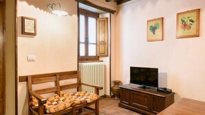 A cozy living room with a wooden bench, a television on a cabinet, and framed artwork on the wall. - Borgo dei Corsi - RIBUSTINO 2 Apartment (Raggiolo)