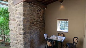 Uma parede de pedra, teto de madeira, uma janela e uma mesa com cadeiras.