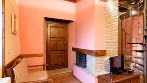 Um quarto acolhedor com porta de madeira, lareira, uma cadeira e televisão sobre um suporte de madeira.