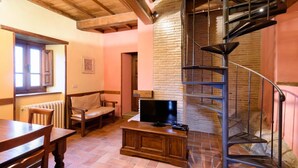 Uma sala de estar aconchegante com uma mesa de madeira, um sofá, uma TV sobre um suporte de madeira e uma escada em espiral em frente a uma parede de tijolos.