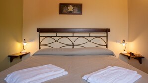 A neatly made bed with two white towels, a wooden headboard, and two bedside lamps on either side.
