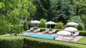A pool area with lounge chairs and umbrellas, surrounded by well-maintained hedges and trees.
