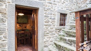 A stone building with a wooden door leading to a dining area with a table and chairs. - Borgo dei Corsi - VERGAIO 6 Apartment (Raggiolo)