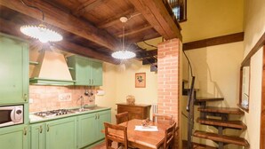 A kitchen with green cabinets, a wooden dining table, and a brick column. - Borgo dei Corsi - VERGAIO 6 Apartment (Raggiolo)