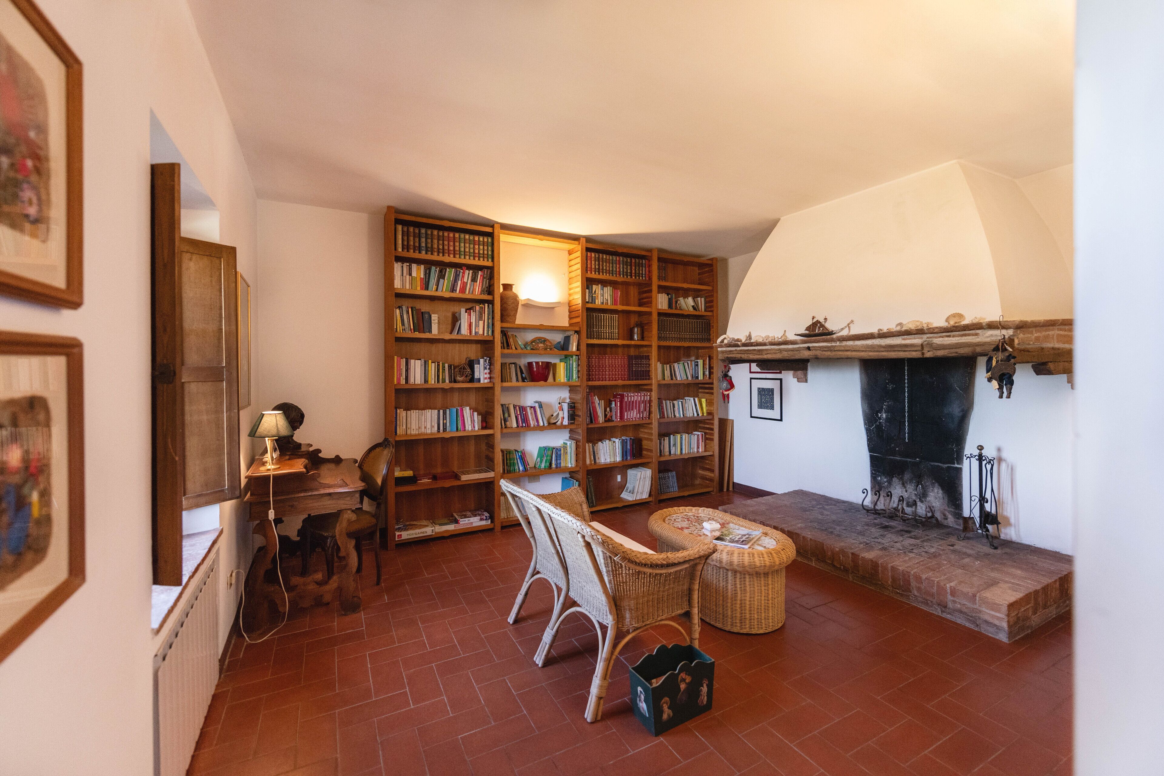 A cozy reading nook with a fireplace, bookshelves, and wicker furniture.