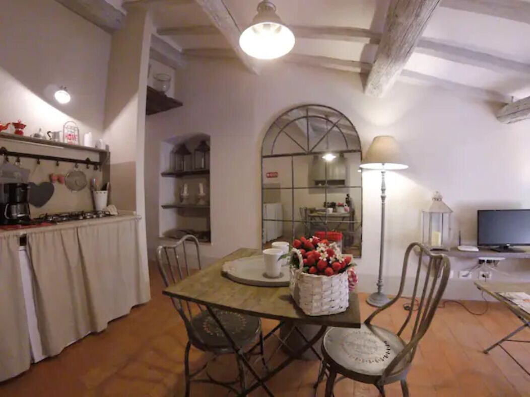 A dining area with a wooden table, chairs, a basket of flowers, and a television in the background.