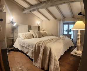 Une chambre à coucher avec un grand lit, une table de chevet, une lampe et une fenêtre avec des rideaux.