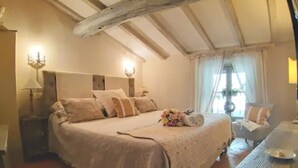 A bedroom with a large bed, a nightstand, a lamp, and a wooden table. - Cortona Shabby Chic House<br>(Independent & balcony) (Cortona)
